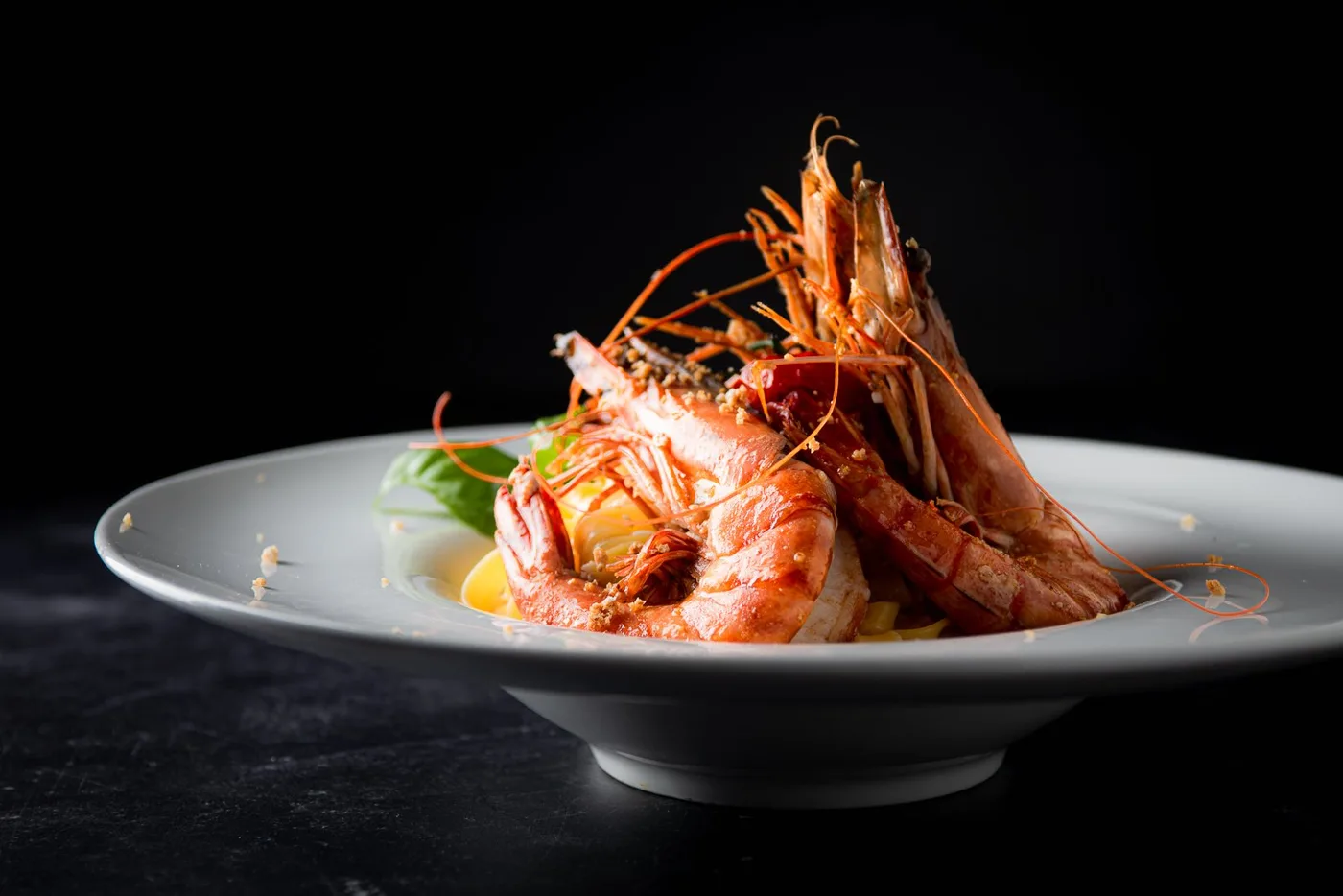 Tagliatelle met gegrilde gamba's en verse kruiden op een diep bord.